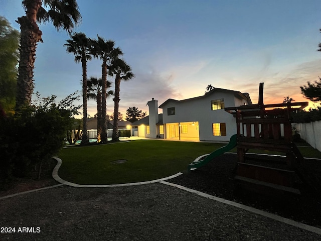 back house at dusk with a playground and a lawn