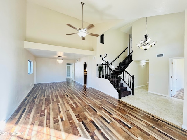 unfurnished living room with hardwood / wood-style floors, high vaulted ceiling, and ceiling fan with notable chandelier