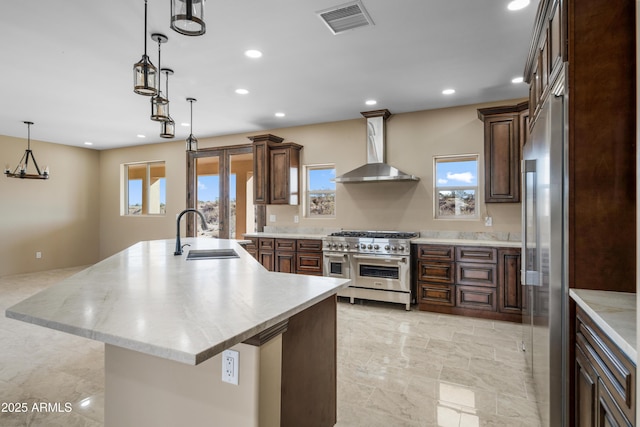 kitchen with wall chimney range hood, sink, decorative light fixtures, a large island, and premium appliances