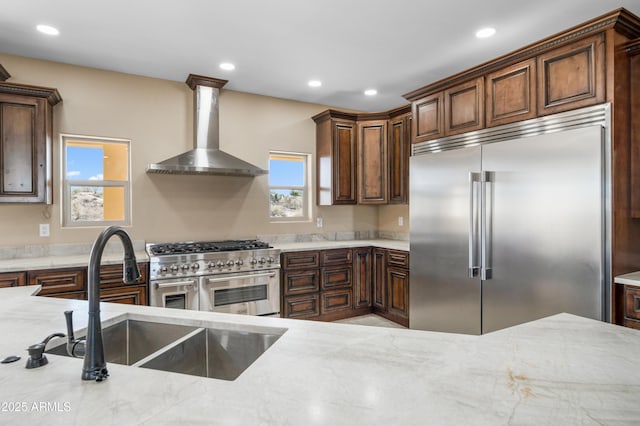 kitchen featuring light stone countertops, sink, high end appliances, and wall chimney range hood