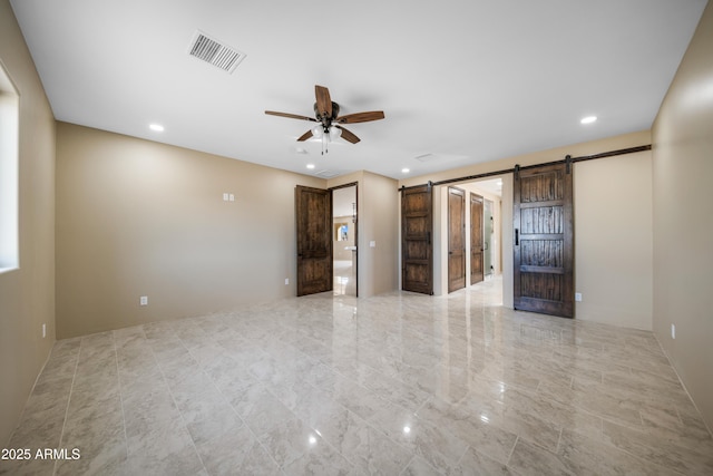 spare room featuring ceiling fan and a barn door