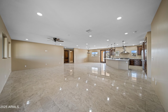 kitchen with ceiling fan, sink, wall chimney exhaust hood, decorative light fixtures, and a kitchen island