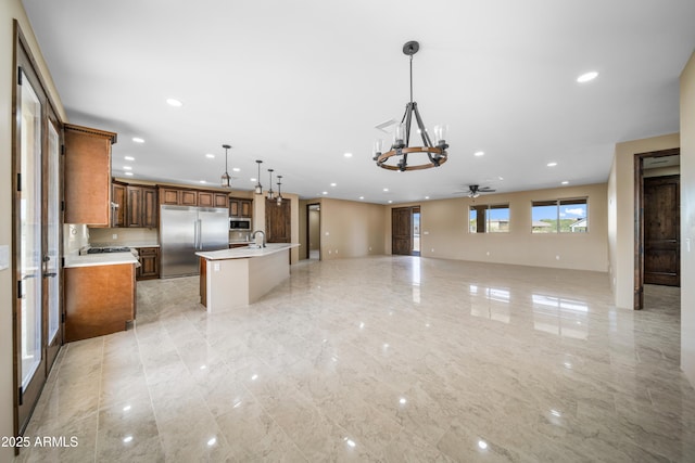 kitchen with a center island with sink, ceiling fan with notable chandelier, sink, decorative light fixtures, and stainless steel appliances