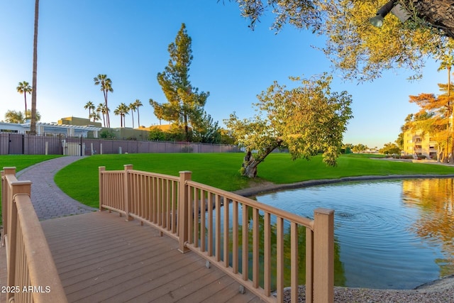 wooden terrace with a lawn, a water view, and fence