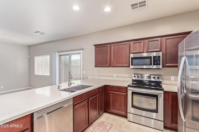 kitchen with appliances with stainless steel finishes, sink, light tile patterned floors, kitchen peninsula, and light stone countertops