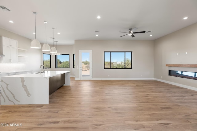 kitchen with light stone countertops, light wood-type flooring, decorative light fixtures, white cabinets, and a kitchen island with sink