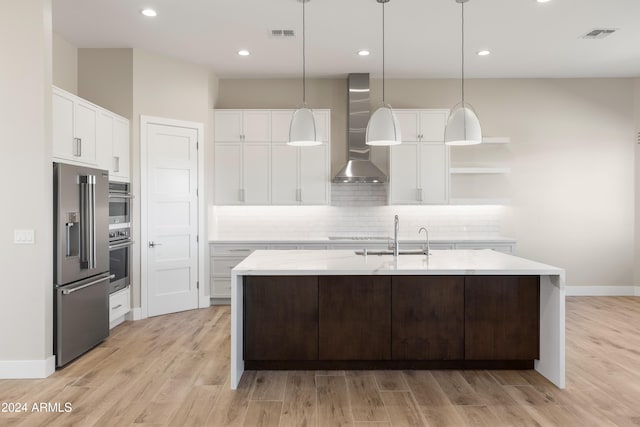 kitchen with white cabinets, wall chimney range hood, sink, and stainless steel fridge