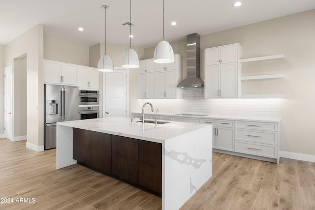 kitchen with appliances with stainless steel finishes, white cabinets, sink, and wall chimney range hood