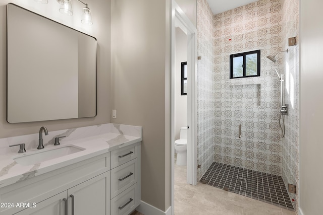 bathroom featuring vanity, a tile shower, toilet, and tile patterned floors