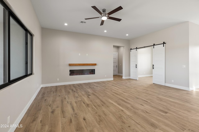 unfurnished living room featuring a barn door, light hardwood / wood-style flooring, and ceiling fan