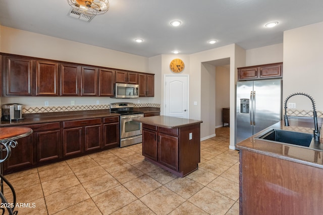 kitchen with light tile patterned floors, stainless steel appliances, a sink, visible vents, and a center island