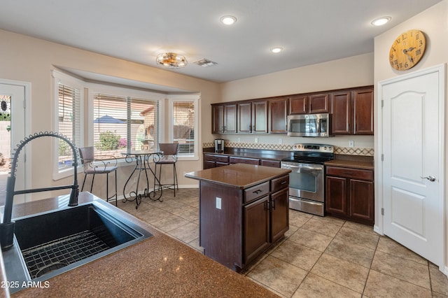 kitchen featuring light tile patterned floors, dark brown cabinetry, stainless steel appliances, a kitchen island, and a sink