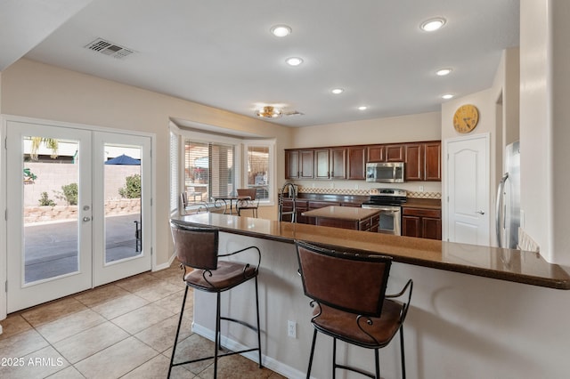 kitchen with light tile patterned floors, visible vents, appliances with stainless steel finishes, a breakfast bar, and french doors