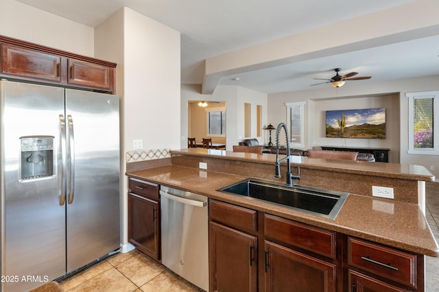 kitchen featuring open floor plan, a peninsula, stainless steel appliances, a sink, and light tile patterned flooring