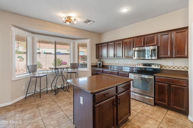 kitchen with stainless steel appliances, light tile patterned flooring, dark countertops, and visible vents