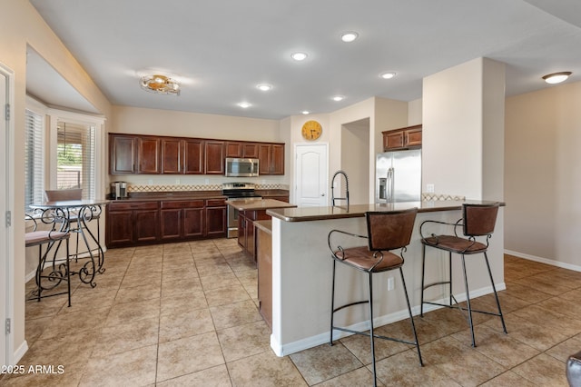 kitchen featuring light tile patterned floors, a breakfast bar area, a sink, appliances with stainless steel finishes, and dark countertops