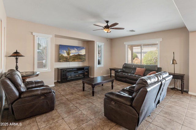 living room featuring light tile patterned floors, baseboards, visible vents, a ceiling fan, and a glass covered fireplace