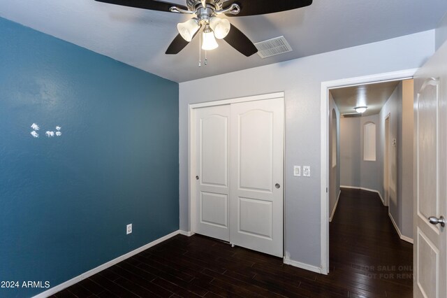 unfurnished bedroom featuring ceiling fan, a closet, and dark wood-type flooring