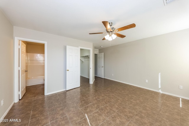 unfurnished bedroom featuring connected bathroom, a ceiling fan, baseboards, a closet, and a walk in closet