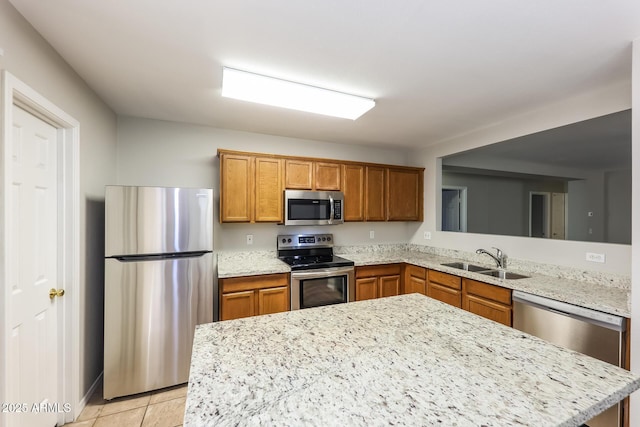 kitchen featuring light stone counters, brown cabinets, light tile patterned floors, appliances with stainless steel finishes, and a sink