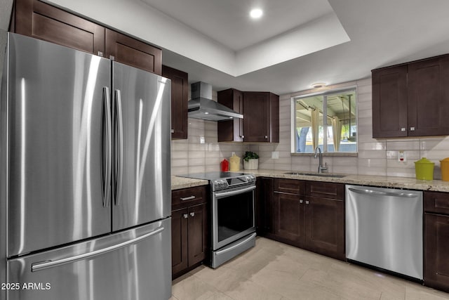 kitchen with wall chimney exhaust hood, sink, appliances with stainless steel finishes, and tasteful backsplash