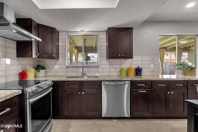 kitchen featuring appliances with stainless steel finishes, light stone counters, wall chimney exhaust hood, and sink