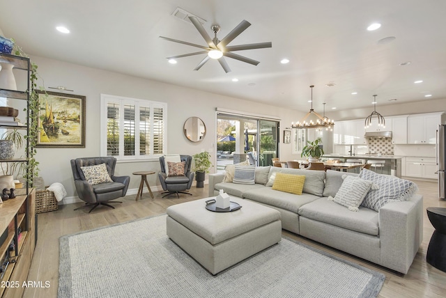 living room featuring ceiling fan with notable chandelier and light hardwood / wood-style floors