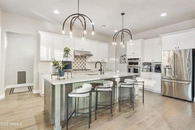 kitchen featuring white cabinetry, stainless steel appliances, hanging light fixtures, and a center island with sink