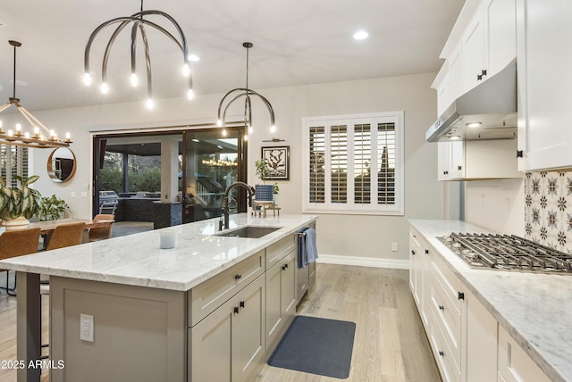 kitchen featuring stainless steel gas cooktop, decorative light fixtures, sink, and a center island with sink