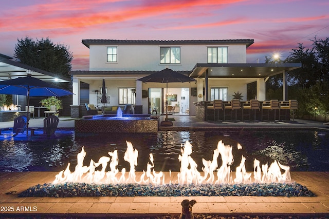 back house at dusk featuring pool water feature and an outdoor fire pit