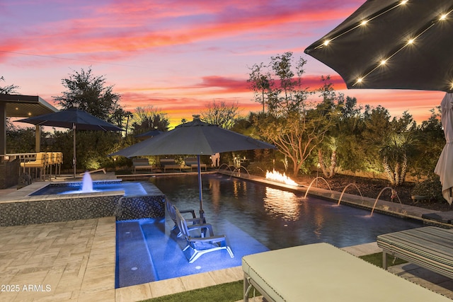 pool at dusk featuring an in ground hot tub, pool water feature, and a patio