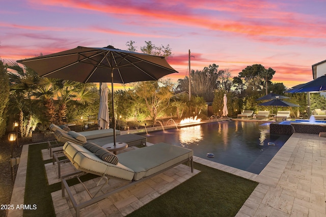 pool at dusk featuring a patio, pool water feature, and an in ground hot tub