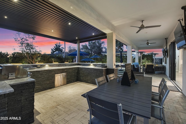 patio terrace at dusk featuring ceiling fan and area for grilling