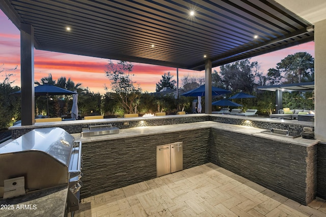 patio terrace at dusk with a gazebo, an outdoor kitchen, and a grill