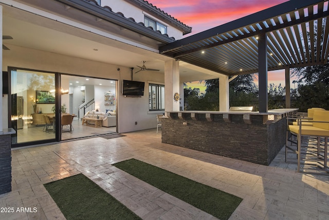 patio terrace at dusk with a bar, ceiling fan, and a pergola