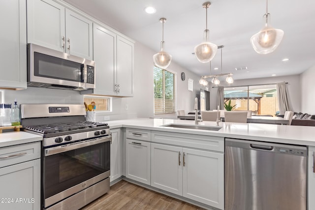 kitchen featuring pendant lighting, appliances with stainless steel finishes, kitchen peninsula, sink, and light wood-type flooring