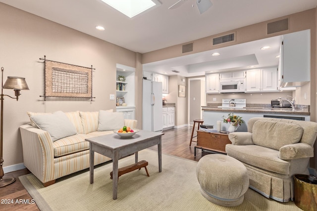 living room featuring a skylight, ceiling fan, and light hardwood / wood-style flooring