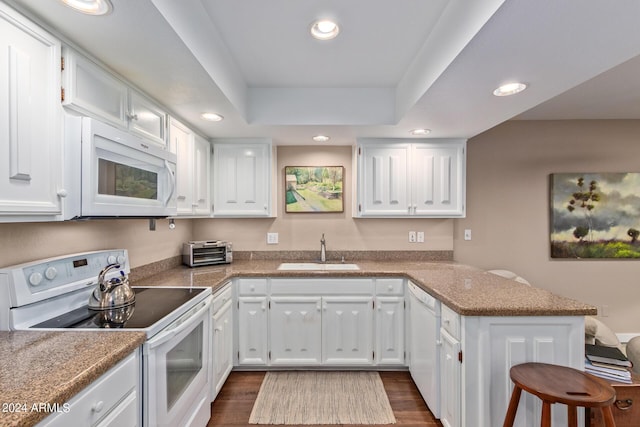 kitchen featuring sink, white appliances, white cabinetry, a raised ceiling, and kitchen peninsula