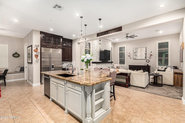 kitchen with ceiling fan, a kitchen island with sink, sink, white cabinetry, and a kitchen bar