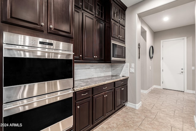 kitchen featuring dark brown cabinetry, light stone countertops, stainless steel appliances, and decorative backsplash