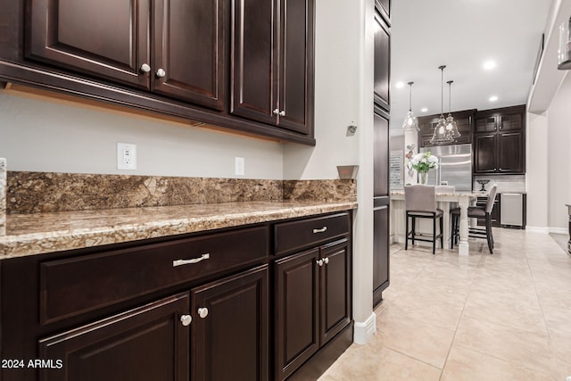 kitchen with dark brown cabinetry, decorative light fixtures, light stone counters, and light tile patterned floors