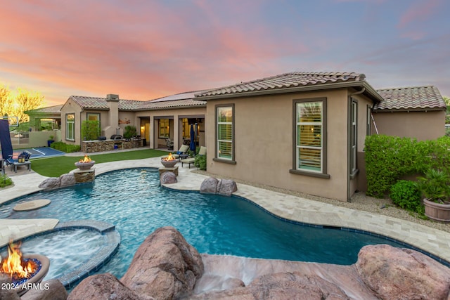 pool at dusk featuring a jacuzzi and a patio area