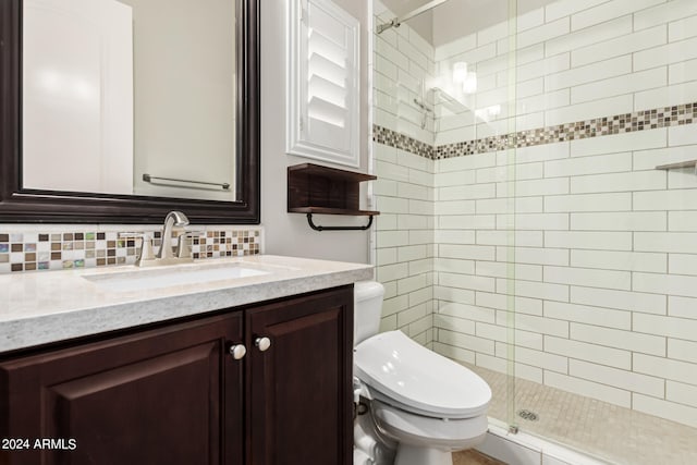 bathroom with backsplash, a shower with door, vanity, and toilet