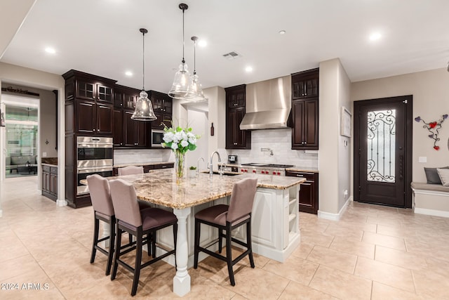 kitchen featuring dark brown cabinetry, tasteful backsplash, sink, wall chimney range hood, and a spacious island