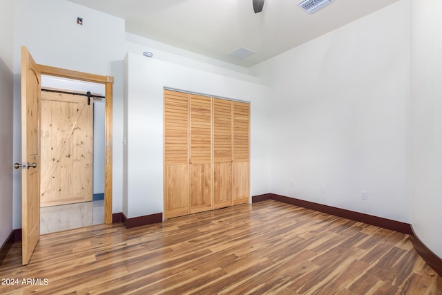 unfurnished bedroom featuring a barn door, dark wood-type flooring, ceiling fan, and a closet