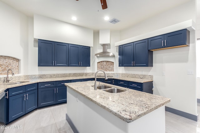 kitchen with blue cabinetry, sink, a kitchen island with sink, and light stone counters