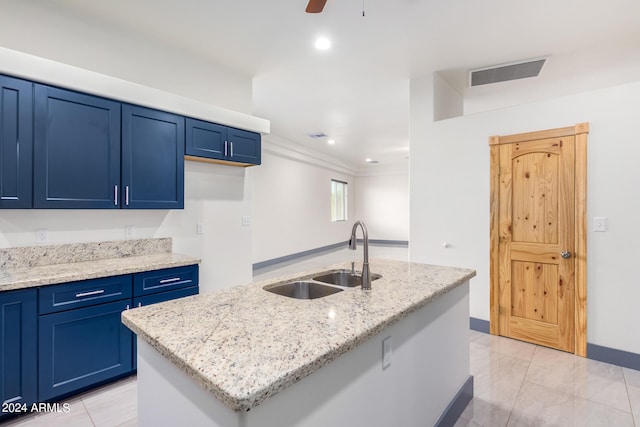 kitchen with a kitchen island with sink, sink, light stone counters, and blue cabinets