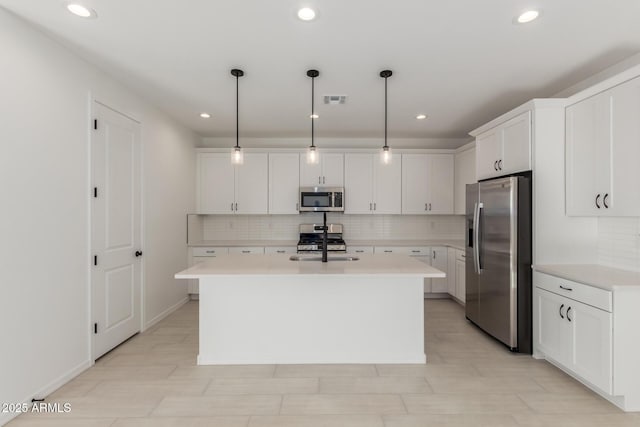 kitchen with white cabinetry, tasteful backsplash, pendant lighting, stainless steel appliances, and a kitchen island with sink