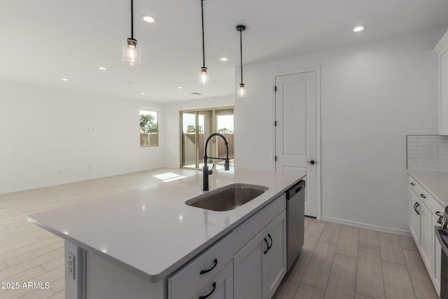 kitchen with pendant lighting, sink, white cabinets, stainless steel dishwasher, and a center island with sink