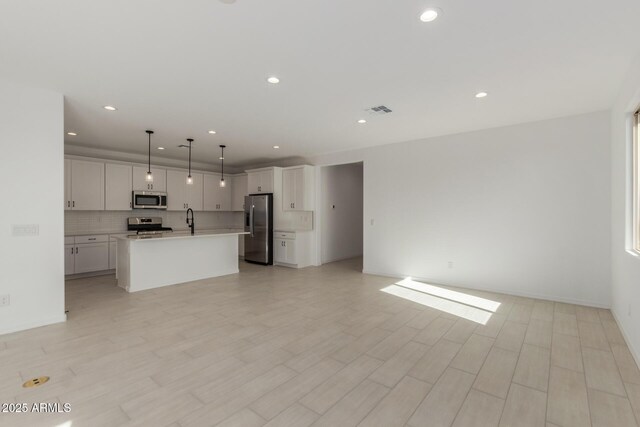 kitchen featuring a center island with sink, pendant lighting, stainless steel appliances, decorative backsplash, and white cabinets